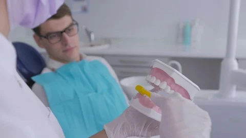 Dentist using jaw mock and toothbrush to teach patient correct cleaning of teeth Stock Footage 95968296
