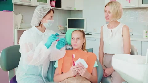 Dentist woman explaining and teaching teen girl patient and her mother in Stock Footage 252321399