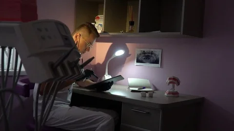 Dentist is working on the tablet in the office with pink walls. Parallax Stock Footage