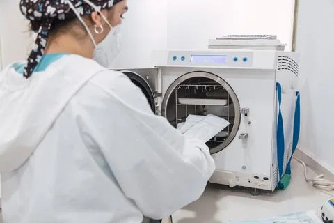 The dentist's assistant insert the packaged dental instrument to the autoclav Stock Photos