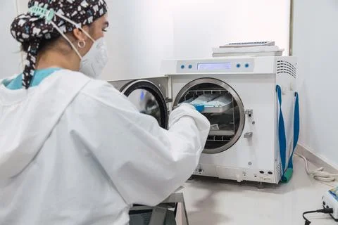 The dentist's assistant insert the packaged dental instrument to the autoclav Foto stock
