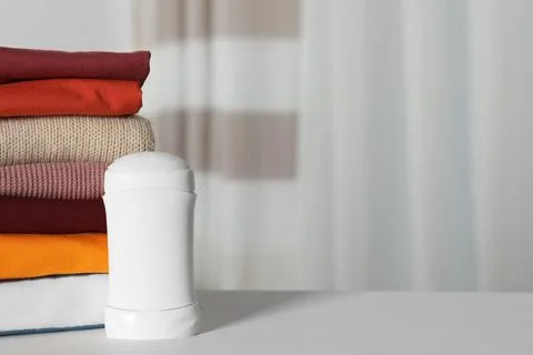 Deodorant near stack of clean clothes on white table. Space for text 스톡 사진