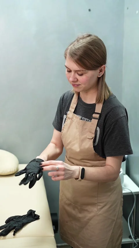 Depilation master puts on black protective gloves before the procedure Video stock 264857724