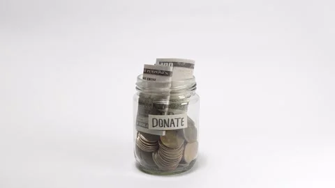 Depositing banknotes into a jar labeled Donate filled with cash and coins Stock Footage 317108692