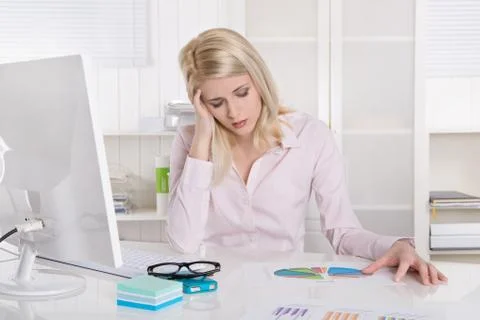 Depressed and frustrated young businesswoman sitting at desk with migraine. Stock Photos