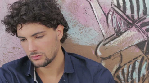 Depressed and sad young man sitting near a graffiti wall Stock Footage 28224073