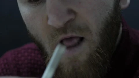 Depressed bearded addict in red pullover licks paper joint Stock Footage 145713842