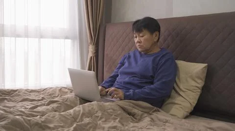 Depressed elderly old Asian woman, people using a notebook laptop computer on Stock Photos
