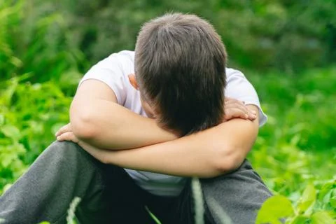 Depressed kid hide head in hands alone in school yard. unhappy boy child bull Stock Photos