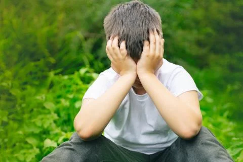Depressed kid hide head in hands alone in school yard. unhappy boy child bull Stock Photos