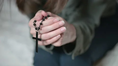 Depressed lady brunette sits on grey sofa and prays holding rosary in hands Stock Footage 157828404