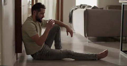 Depressed man drinking alcohol sitting on floor in apartment Stock Footage 271161237