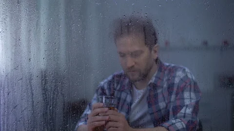 Depressed man drinking whiskey alone on rainy day, thinking about life problems Stock Footage 107215791