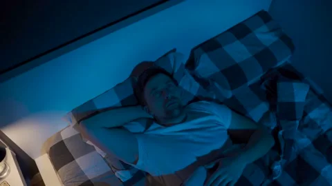 Depressed man lying in bed cannot sleep from insomnia. Young male trying to Stockbeeldmateriaal 145439696