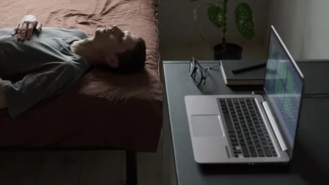 Depressed man lying on bed in despair in home office next to open laptop and Stock-Footage 309908696