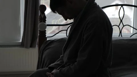 Depressed man sitting on bed in dark room, burnout and mental health concept Видео 332055726