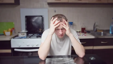 Depressed man sitting at home at the table, clasping his head with his hands Stock Footage 134936870