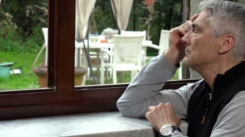Depressed middle aged man looking out the window in a boring afternoon at home Stock Footage 74684069