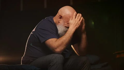 Depressed middle-aged man sits on bed crying, coping with midlife crisis Stock Footage 346714295