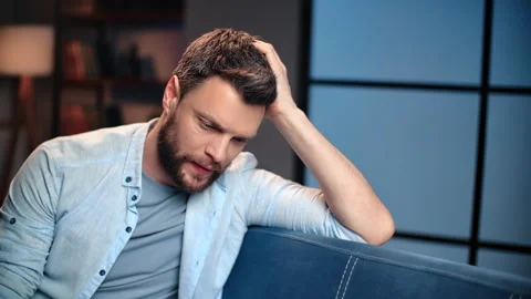 Depressed middle-aged man sitting on couch in apartment at night, thinking about Stock Footage 279770046