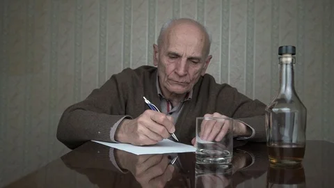 Depressed old man writes on white sheet of paper with pen Stock Footage 126770009