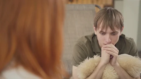 Depressed young man sitting in the office of psychologist, telling her about his Stock Footage 111333232