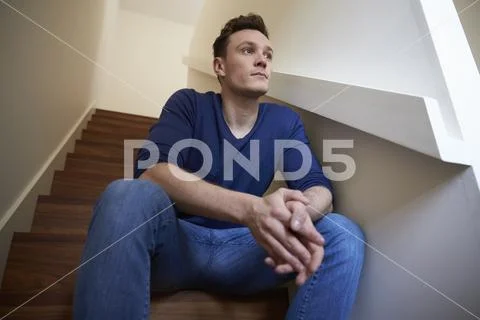 Depressed Young Man Sitting On Stairs At Home