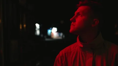 Depressed young man standing on the dark street at night and looking on the red Видео 108123725