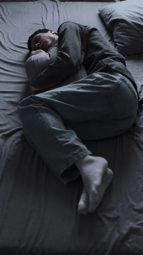 Depression despair young man lying alone on bed hugging pillow feeling emotional Stock Footage 313950597