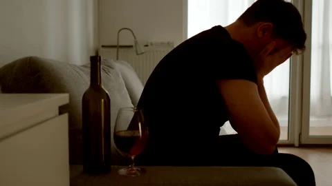 DEPRESSION: Mental suffering of a man on a sofa in a dim room. Alcohol nearby Stock Footage 168681153