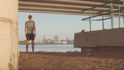 Depressive young man under the bridge, against the background of the evening 스톡 동영상 93821499