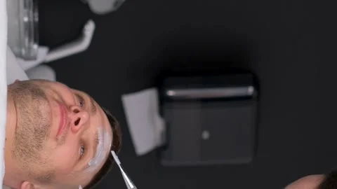 A dermatologist wearing gloves puts a mask on a man's face. Vertical video Stock Footage 250356530
