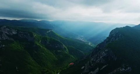 Descend Through Mountain Crevice Sharp Cliffs Reveal Small Houses Road Drone Video stock 300479878