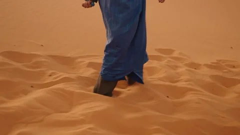 A desert guide in blue robe walks barefoot on golden Sahara sands of Morocco Stock Footage 315768721