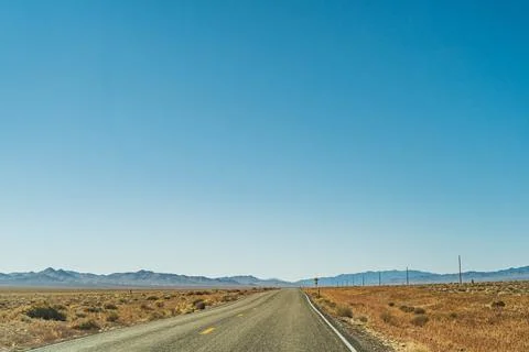 Desert highway road leading to the horizon against clear blue sky and mountains Stock Photos