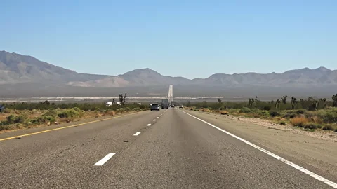 Desert highway through dry mountain landscape under clear blue sky, cars and 库存影片 333838808