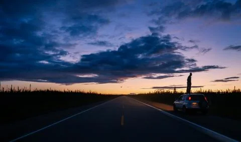 Deserted highway at dusk, man silhouetted on top of car Stock Photos