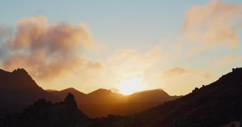 Deserted mountains at sunset. Sun rays illuminate rocks. Cloudy colourful sky in Stock Photos