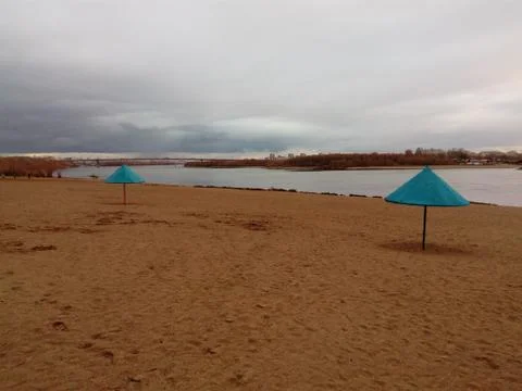 Deserted spring beach. Two beach umbrellas. Gray clouds. Stock Photos