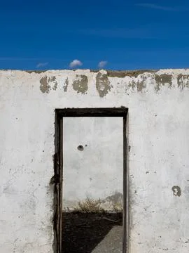 Deserted white wall with doorway frame reveals a barren outdoor scene under a Stock Photos