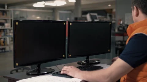 Design engineer works on a computer behind monitors in a machine shop. Stock Footage 265509792