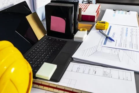 A design engineer's desk with construction drawings, a laptop, and material.. 写真素材
