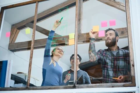 Design team writing on adhesive notes and drawing on design studio window Foto stock