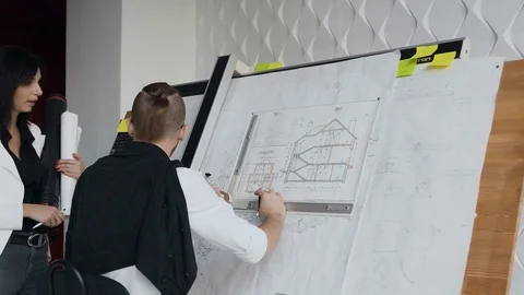 The designer and engineer stand next to the drawing instrument with the project Stock Footage 83031759