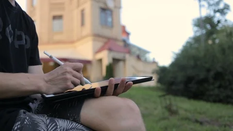 Designer drawing a sketch on tablet using stylus at park Stockbeeldmateriaal 92581173