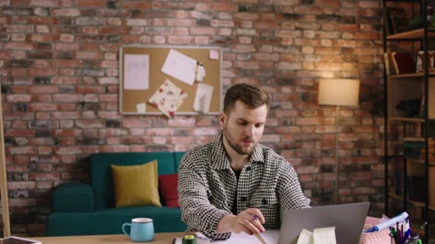A designer man is working at his table in his very homey looking workspace Video stock 194275427