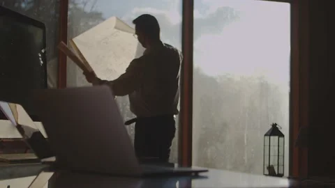 The designer is standing at a large window, unrolling the design plans to Stock Footage 182803095