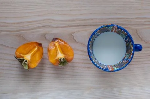 Designer teacup in blue pattern, filled with milk and juicy persimmon cut i.. 写真素材