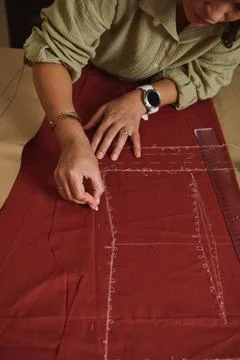 Designer transfers a sewing pattern onto red fabric with tailor's chalk and.. Stock Photos