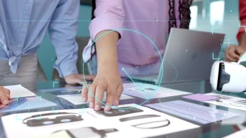 Designers leaning over glass table, pink shirt tapping mockup causing teal holo Stock Footage 333632031